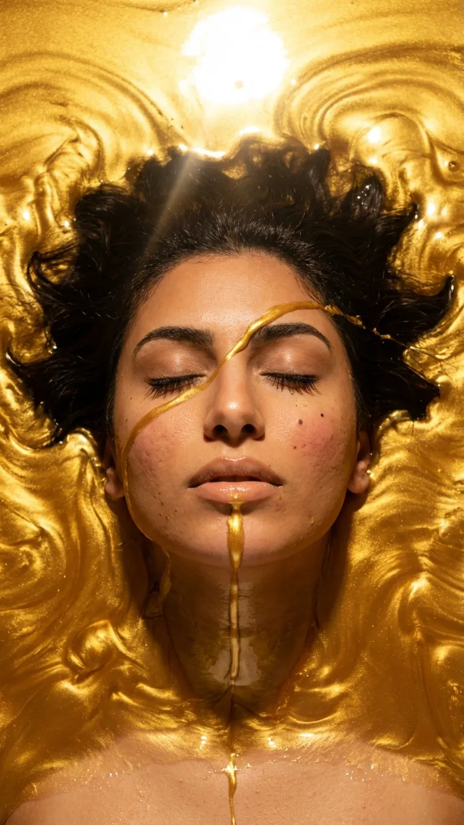 Editorial portrait of a Middle Eastern woman submerged in liquid honey-gold with closed eyes and gold streaming over her face and lips, overhead key light creating a corona around her hair