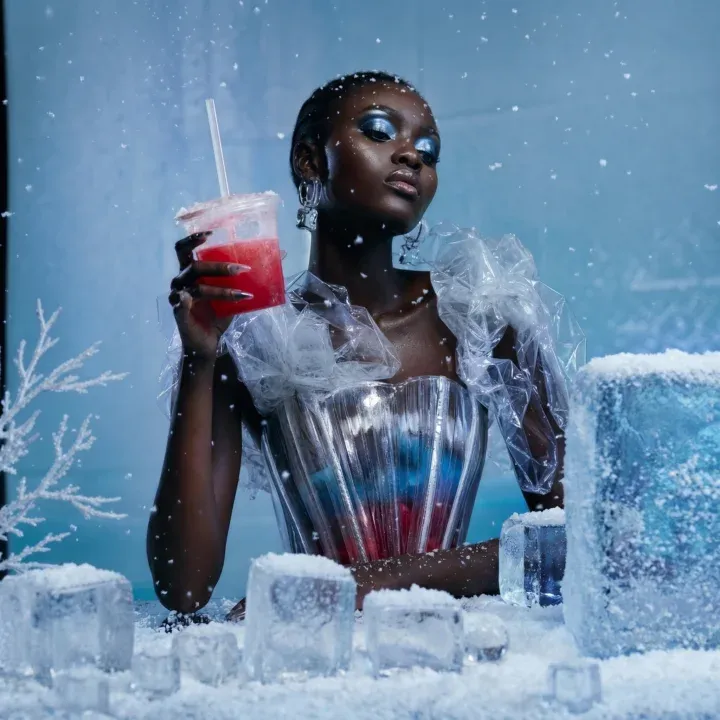 AI-generated portrait of a woman in a sparkling silver bustier sipping a red slushie at an ice-block bar surrounded by snowflakes and frosted branches
