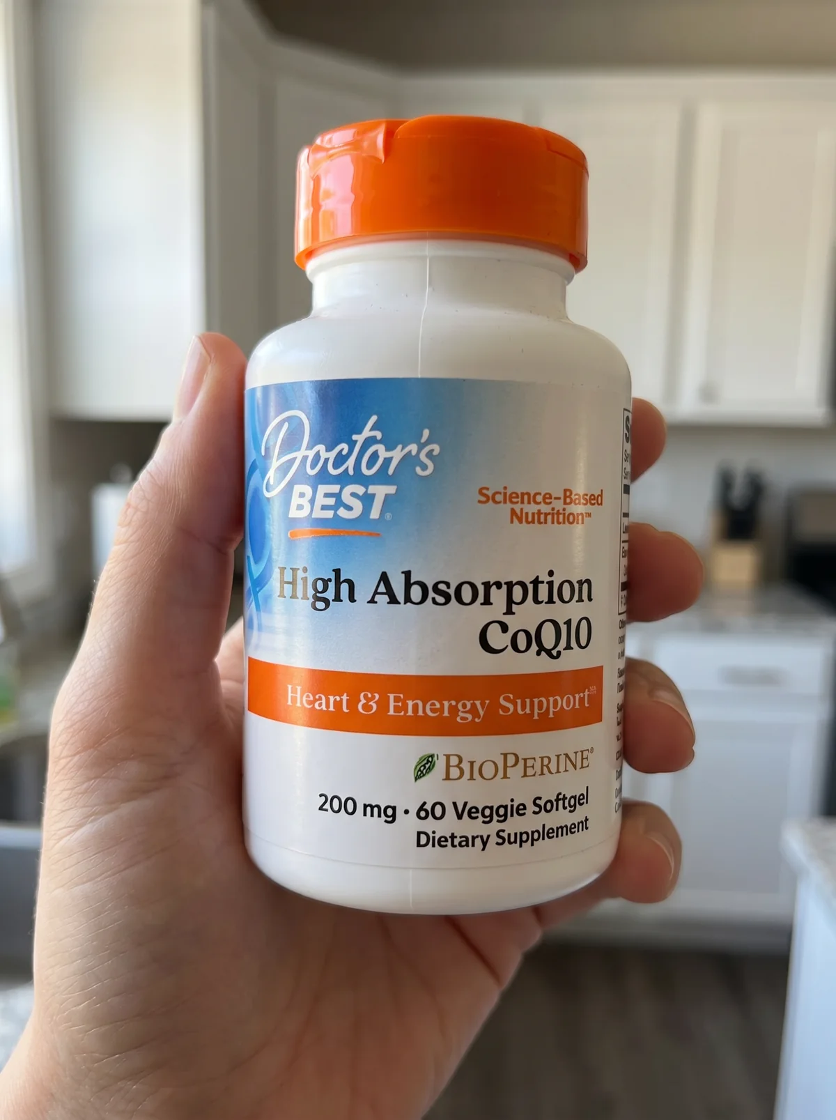 The same supplement bottle held in a hand in a bright kitchen, with the front label fully visible and unobstructed