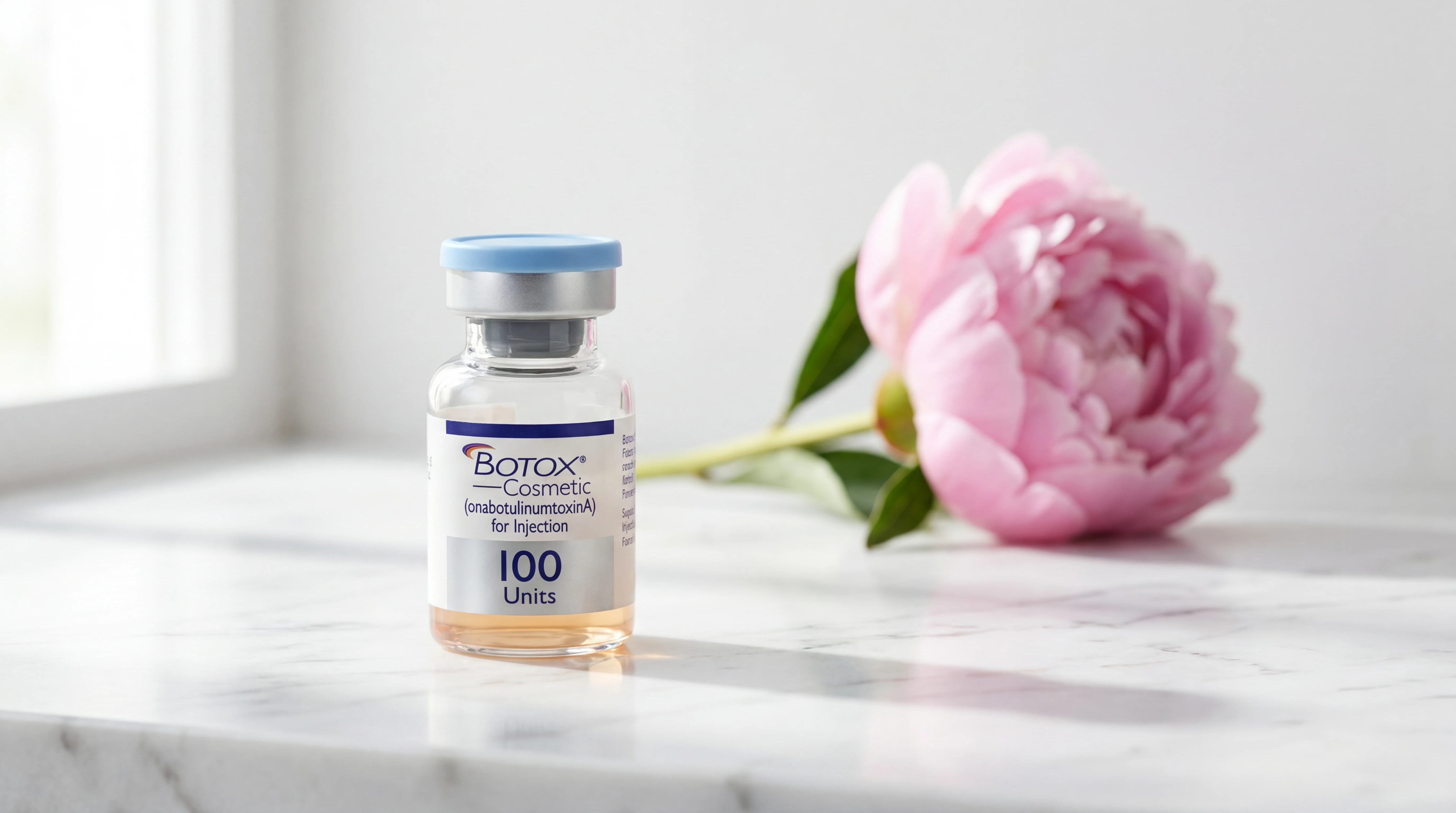 Hyperrealistic luxury product photography of a single 100-unit Botox Cosmetic vial standing upright on white Carrara marble countertop next to a fresh-cut pink peony stem, soft daylight from a window creating gentle highlights and natural shadows, editorial luxury beauty magazine aesthetic