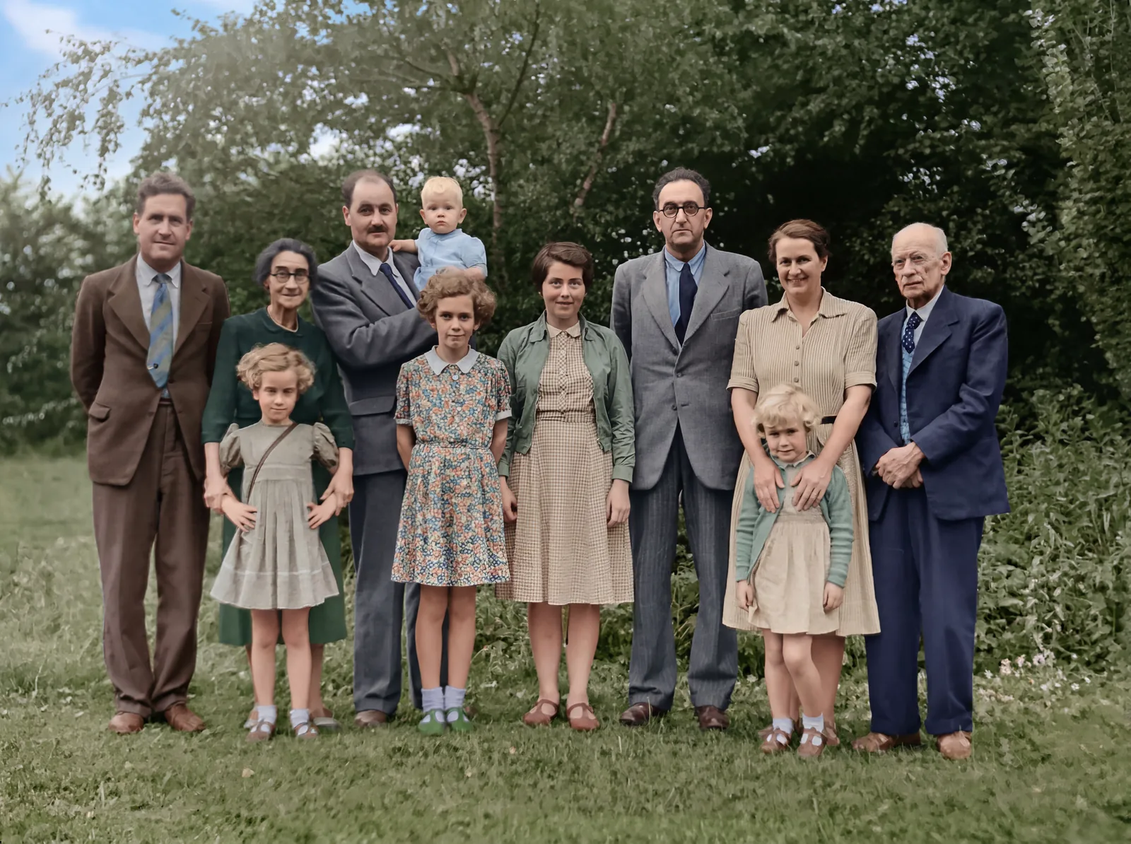 After: the same garden group photo colorized, with green foliage, period-accurate clothing colors, and clearer faces