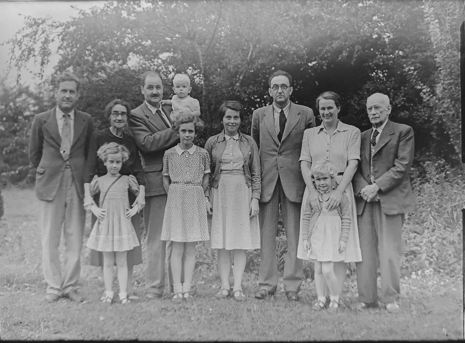 Before: a black-and-white photo of a large group of people in 1920s clothing relaxing on a lawn in a garden