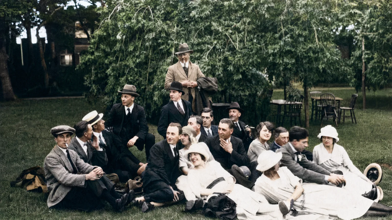 After: the same family portrait colorized, with natural skin tones, varied clothing colors, and green hedges behind, every face preserved